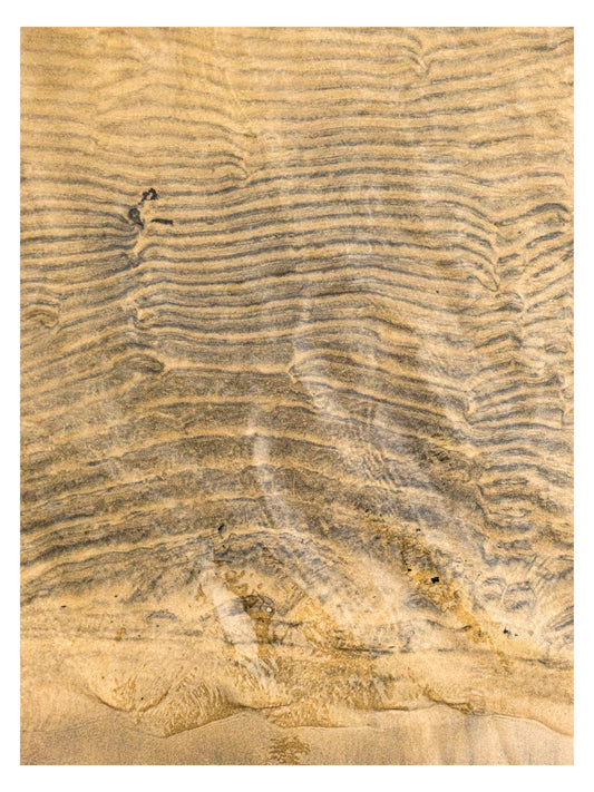 brown sand with current lines under shallow shoreline water.