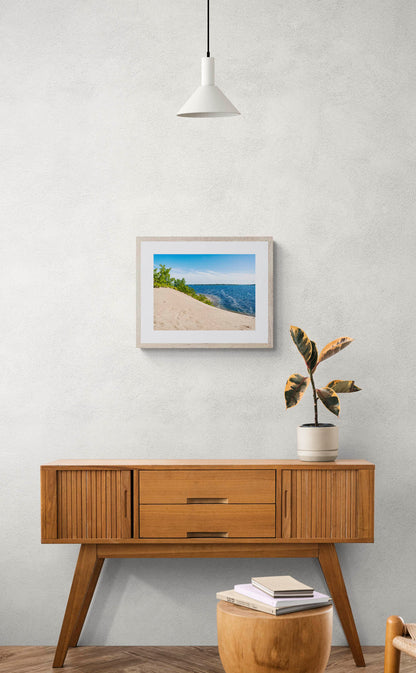mockup of framed sand dune with water photo hanging above wooden console table.
