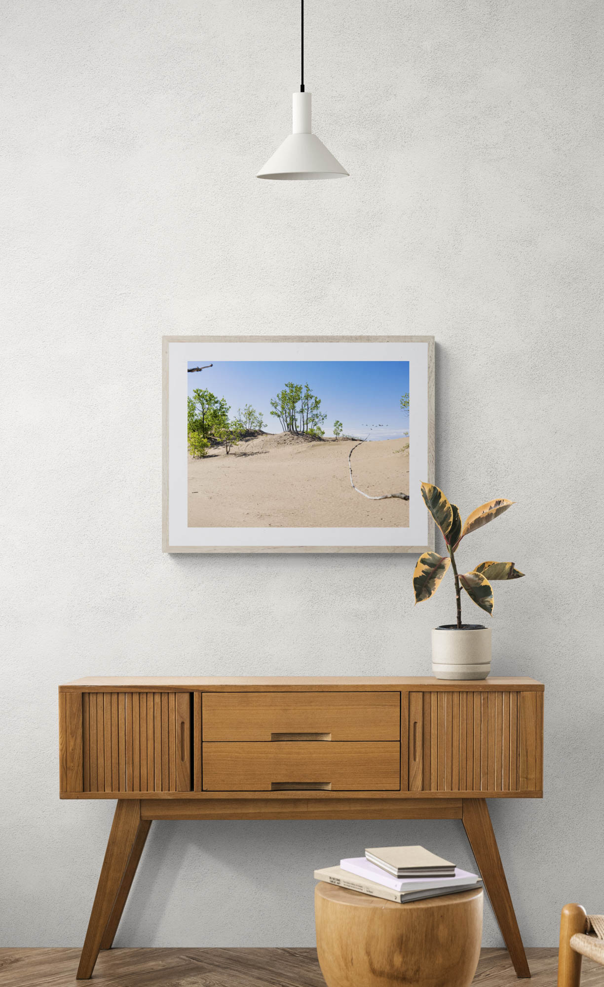 mockup of framed photo of sand and trees hanging above wooden console table.