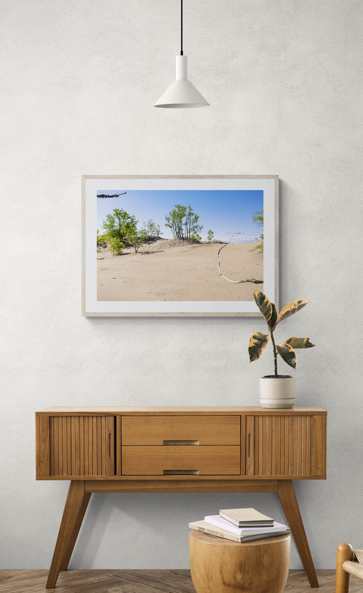 mockup of framed photo of sand and trees hanging above wooden console table.