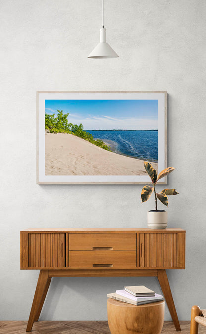 mockup of framed sand dune with water photo hanging above wooden console table.