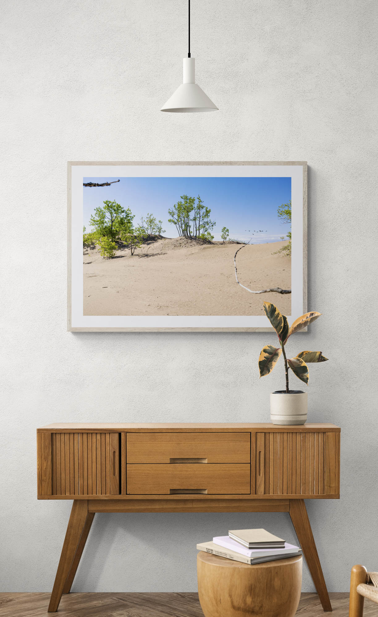 mockup of framed photo of sand and trees hanging above wooden console table.